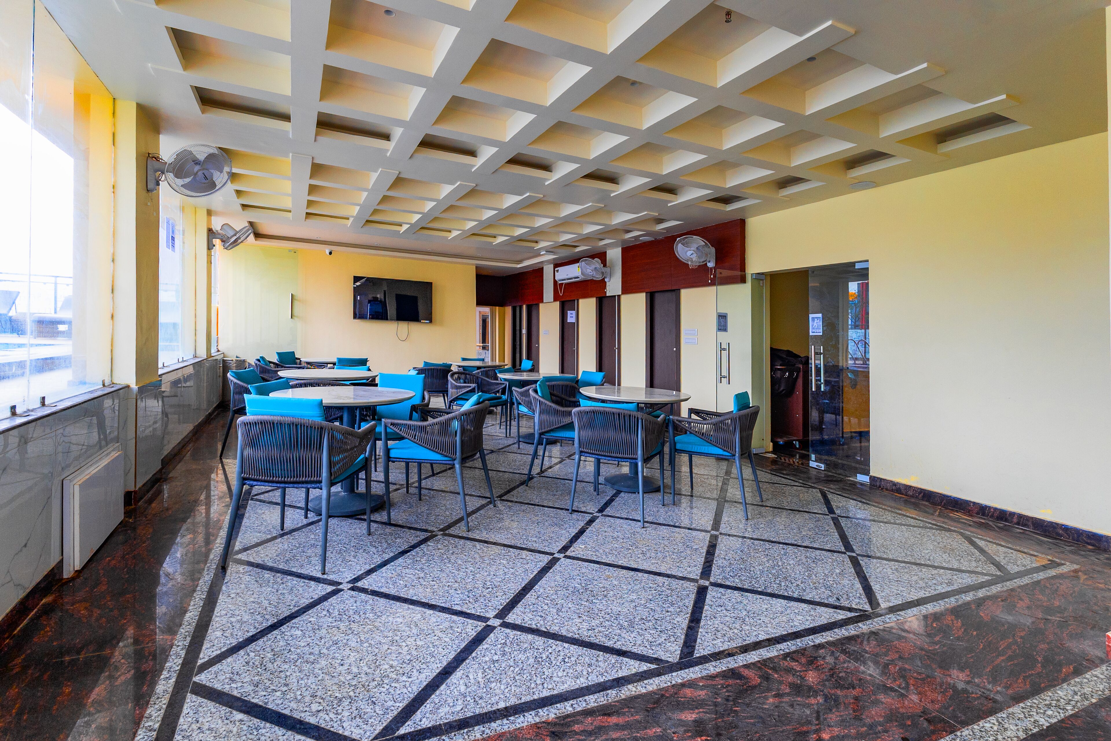 A modern indoor seating area with a geometric patterned floor, multiple tables and chairs, and ceiling fans.