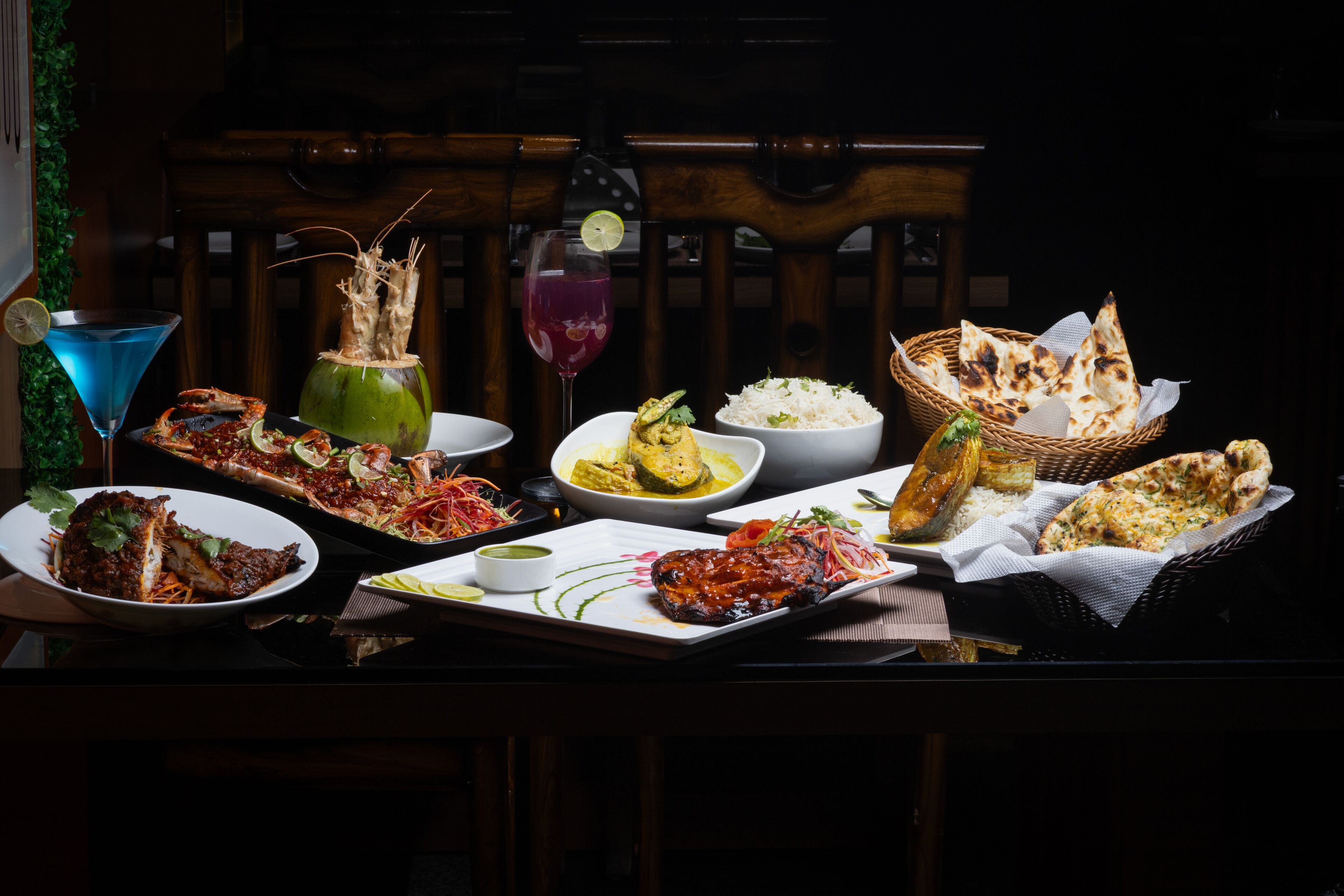 A table set with various dishes, including rice, curry, and grilled meat, along with drinks and bread.