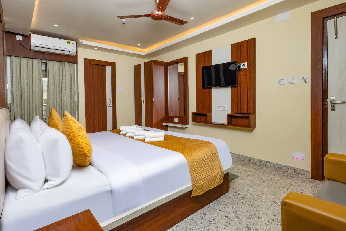A hotel room with a bed, a ceiling fan, a TV mounted on the wall, and a wooden wardrobe.