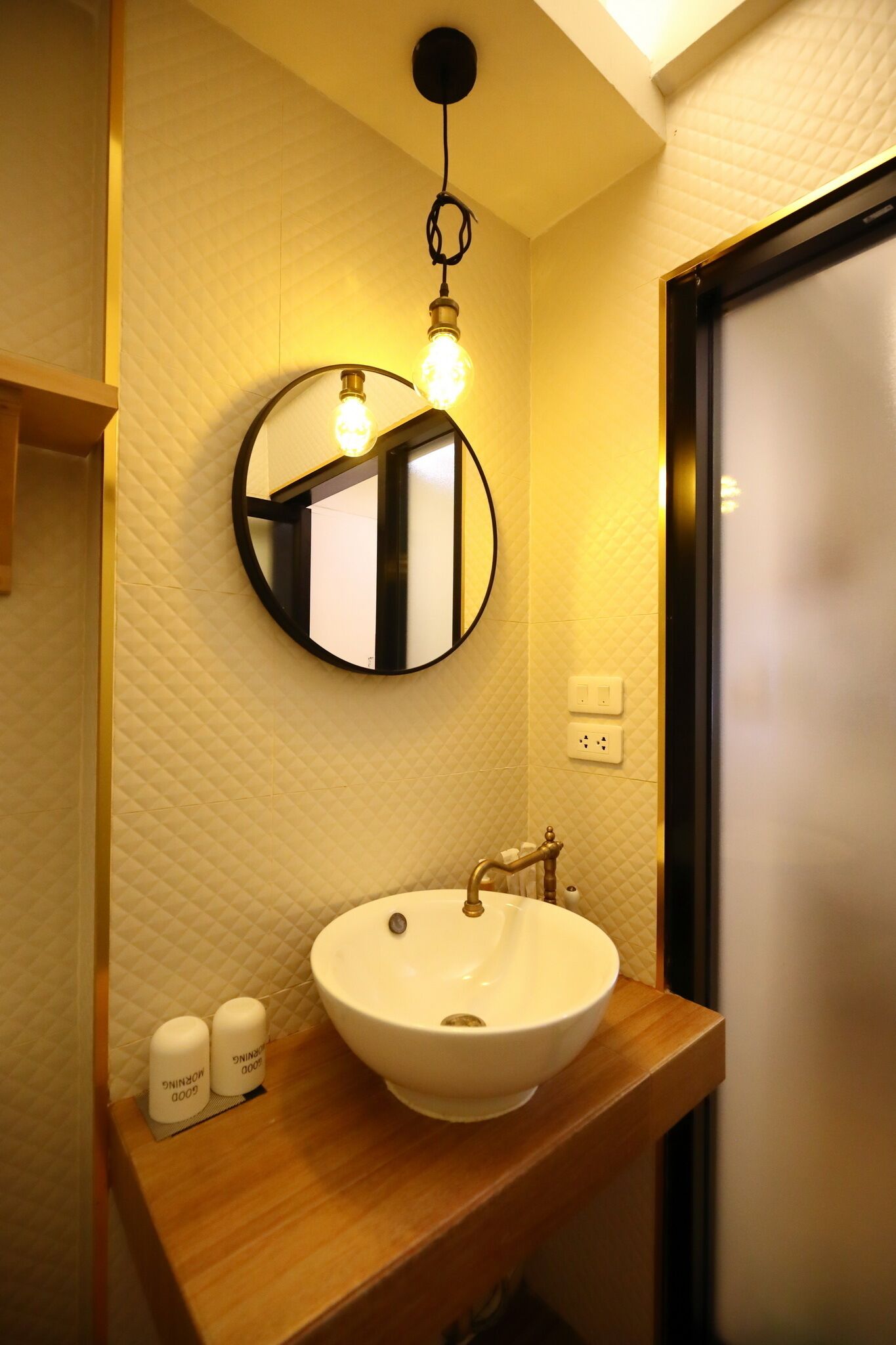 Un baño con un espejo redondo, un lavabo blanco y dos botellas de jabón para manos sobre la encimera.