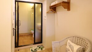 A room with a sliding glass door leading to a bathroom, a wicker chair, and a wooden shelf. - Poshtel Haven (Chiang Mai)