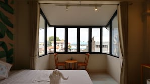 A hotel room with a large bed, two chairs, a small table, and a view of the city through large windows. - Poshtel Haven (Chiang Mai)