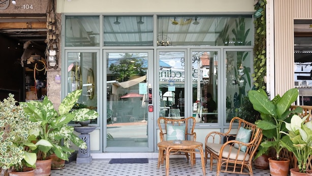 A storefront with a glass door, potted plants, wicker furniture, and a tiled floor. - Poshtel Haven (Chiang Mai)