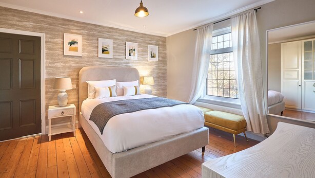 Een moderne slaapkamer met een groot bed, nachtkastjes, een bankje en kunst aan de muur.