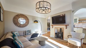 Een woonkamer met een bank, fauteuil, rond bijzettafeltje en een open haard.