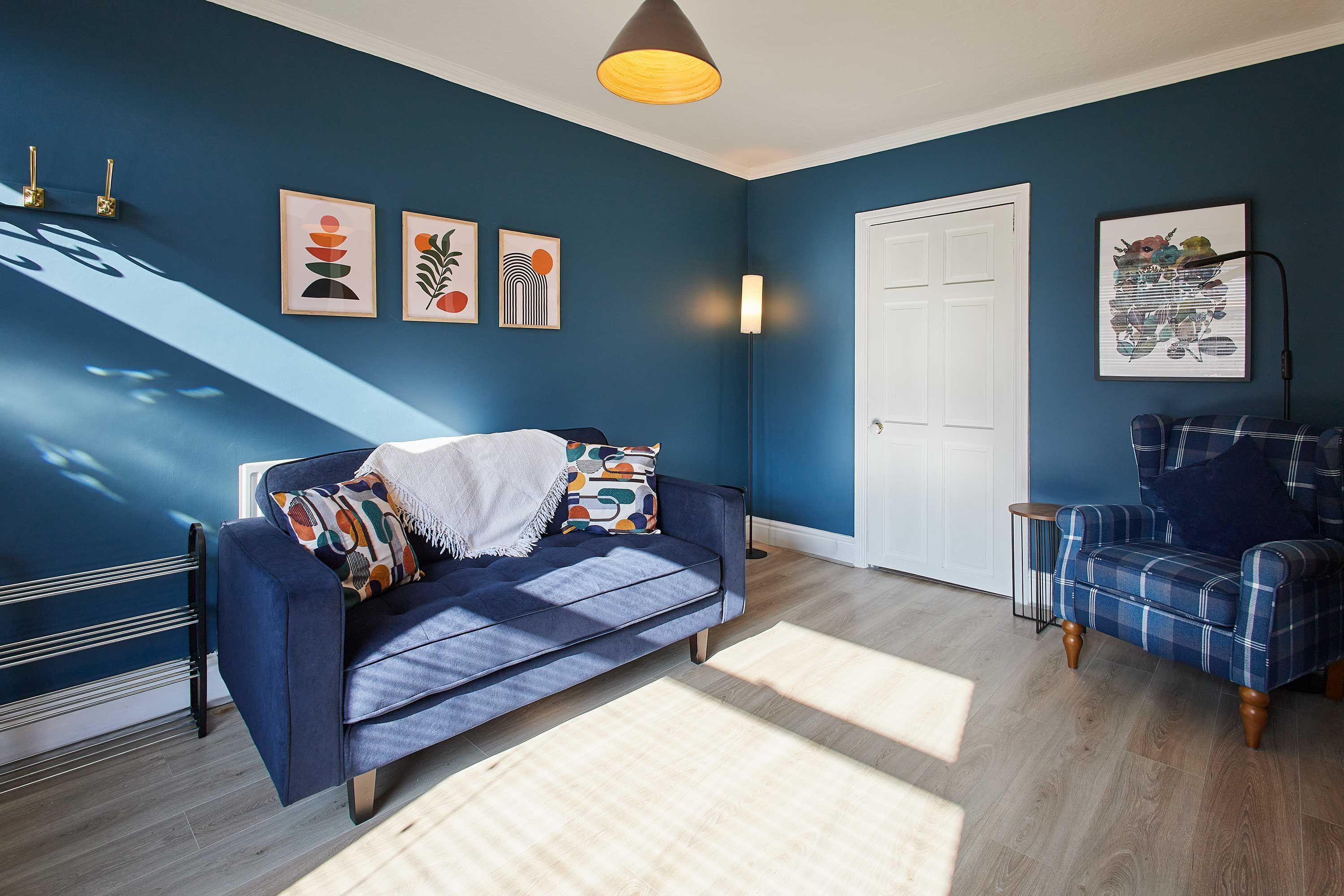 Habitació amb una paret blava, un sofà blau, una butaca escocesa i una porta.