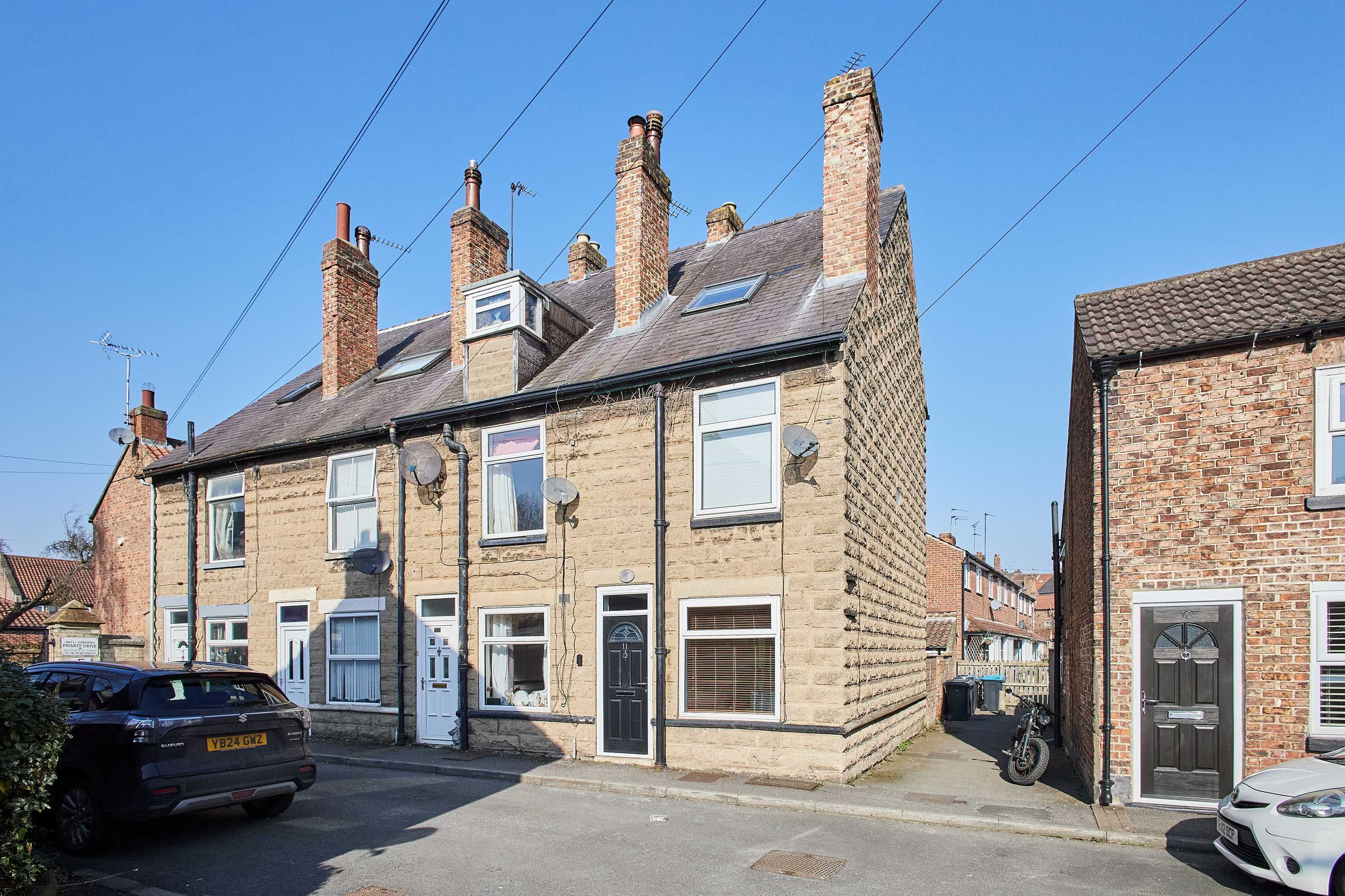 A two-story residential building with brick walls, multiple chimneys, and satellite dishes.