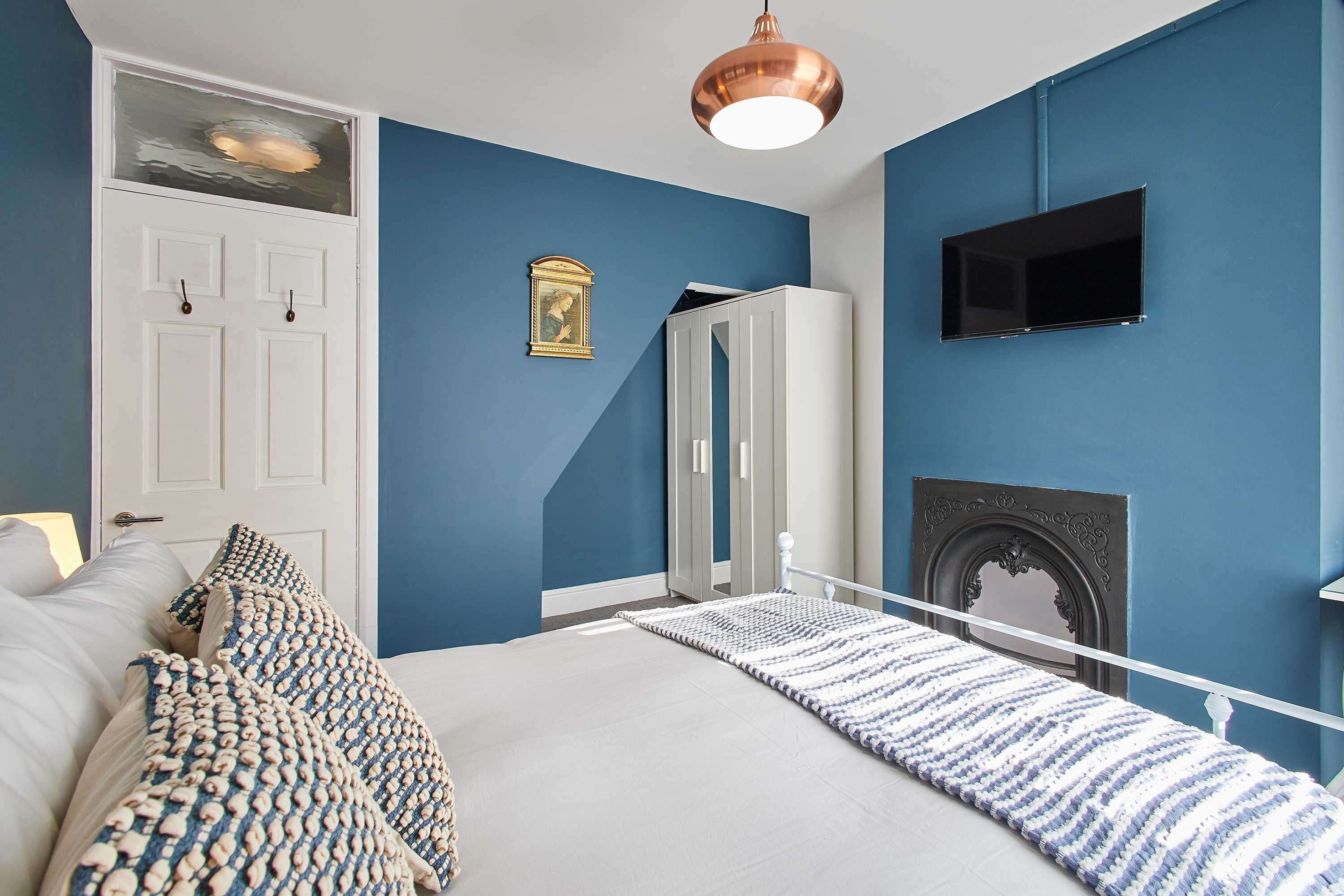 A bedroom with a bed, white wardrobe, TV, and fireplace.