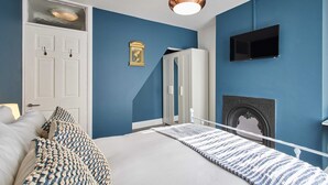 Quarto com cama, guarda-roupa branco, televisão e lareira.