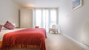 Un dormitorio con cama, una silla, armario y ventana con cortinas.