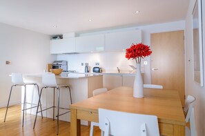 Una cocina moderna con armarios blancos, una mesa de comedor de madera y taburetes de bar.