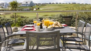 Mesa de desayuno lista con zumo de naranja, pan y un bol, con vista a un campo de golf.