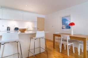 A modern kitchen with white cabinets, a wooden dining table, and bar stools. - Cinq 5 Zinc is a contemporary and inviting two-bedroom apartment (Newquay)