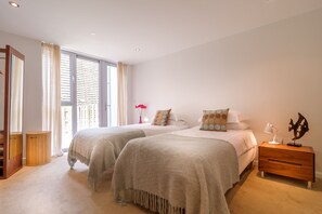 Un dormitorio con dos camas, una mesita de noche de madera, un espejo y una ventana con cortinas.