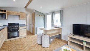 Une cuisine moderne dotée d’appareils électroménagers intégrés, un coin repas avec une table en bois et un téléviseur posé sur un meuble en bois.
