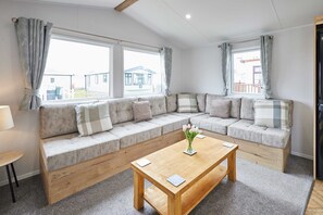 A cozy living room with a sectional sofa, a wooden coffee table, and large windows with curtains. - Host Stay Bowland (Morecambe)