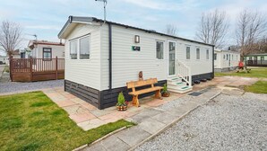 Une maison mobile dotée d’une véranda, d’un banc et d’un petit jardin.