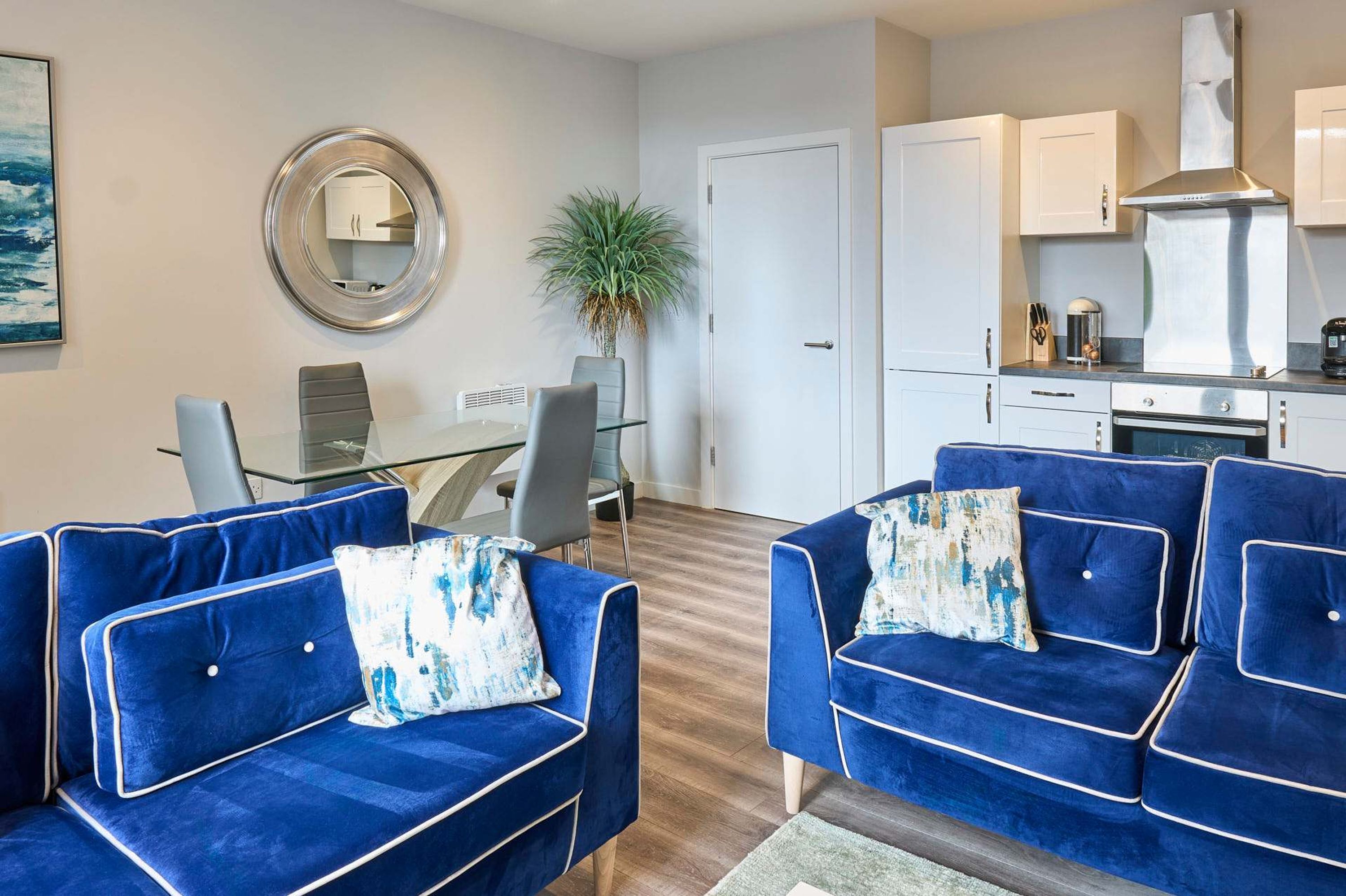 A modern living room with blue sofas, a dining table, and a kitchen area.