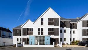 A modern two-story residential building with a prominent blue gate, white walls, and wooden window frames.