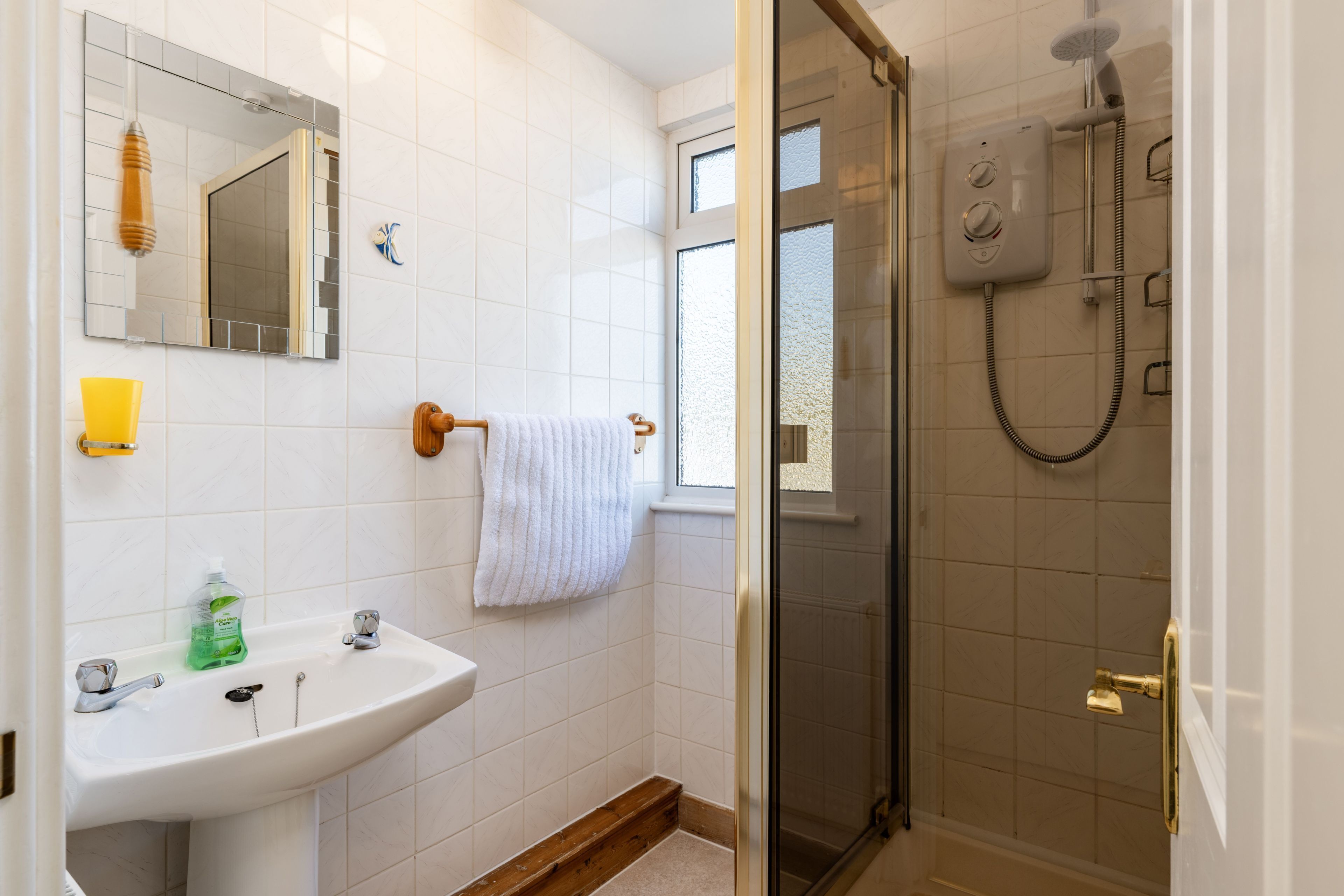 Un bany amb un lavabo blanc, mirall i una cabina de dutxa de vidre.