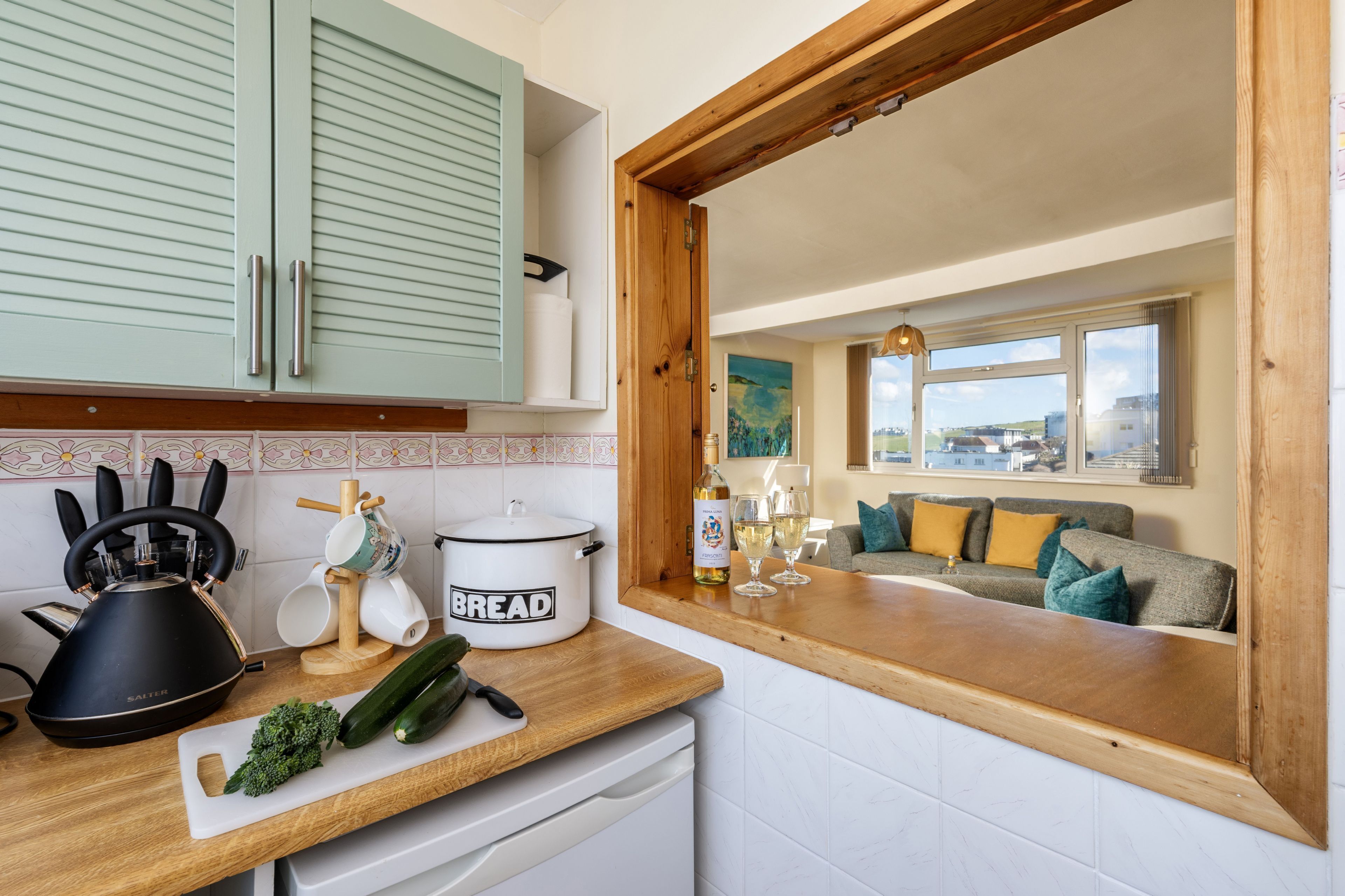 Una cocina con mostrador de madera, un hervidor negro, una panificadora y una tabla de cortar con verduras.