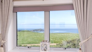 Una finestra vista su un paesaggio erboso e il mare.