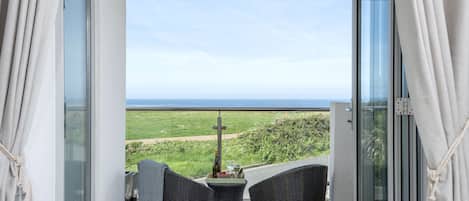 Een balkon met rieten stoelen, een tafeltje en een fles wijn.