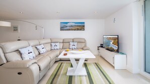 Ein modernes Wohnzimmer mit einem beigefarbenen Sofa, einem weißen Couchtisch und einem Flachbildfernseher.