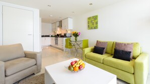 A modern living room with a sofa, a coffee table with fruit, a dining area with chairs, and a kitchen in the background. - 28 Rocklands, a stylish and contemporary Cornish escape (Newquay)