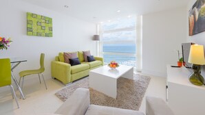 A modern living room with a green sofa, white coffee table, and a view of the sea. - 28 Rocklands, a stylish and contemporary Cornish escape (Newquay)