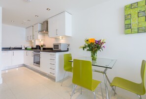 A modern kitchen with white cabinets, a glass table, and green chairs. - 28 Rocklands, a stylish and contemporary Cornish escape (Newquay)