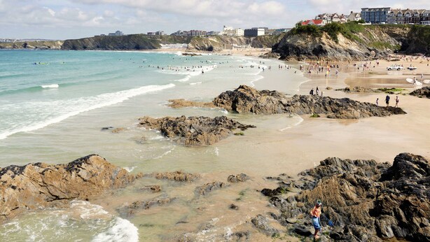 A coastal beach with rocky areas, a sandy shore, and buildings in the background. - 8 Spinnakers, a charming two-bedroom apartment located in Pentire (Newquay)