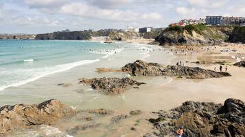A coastal beach with rocky areas, a sandy shore, and buildings in the background.