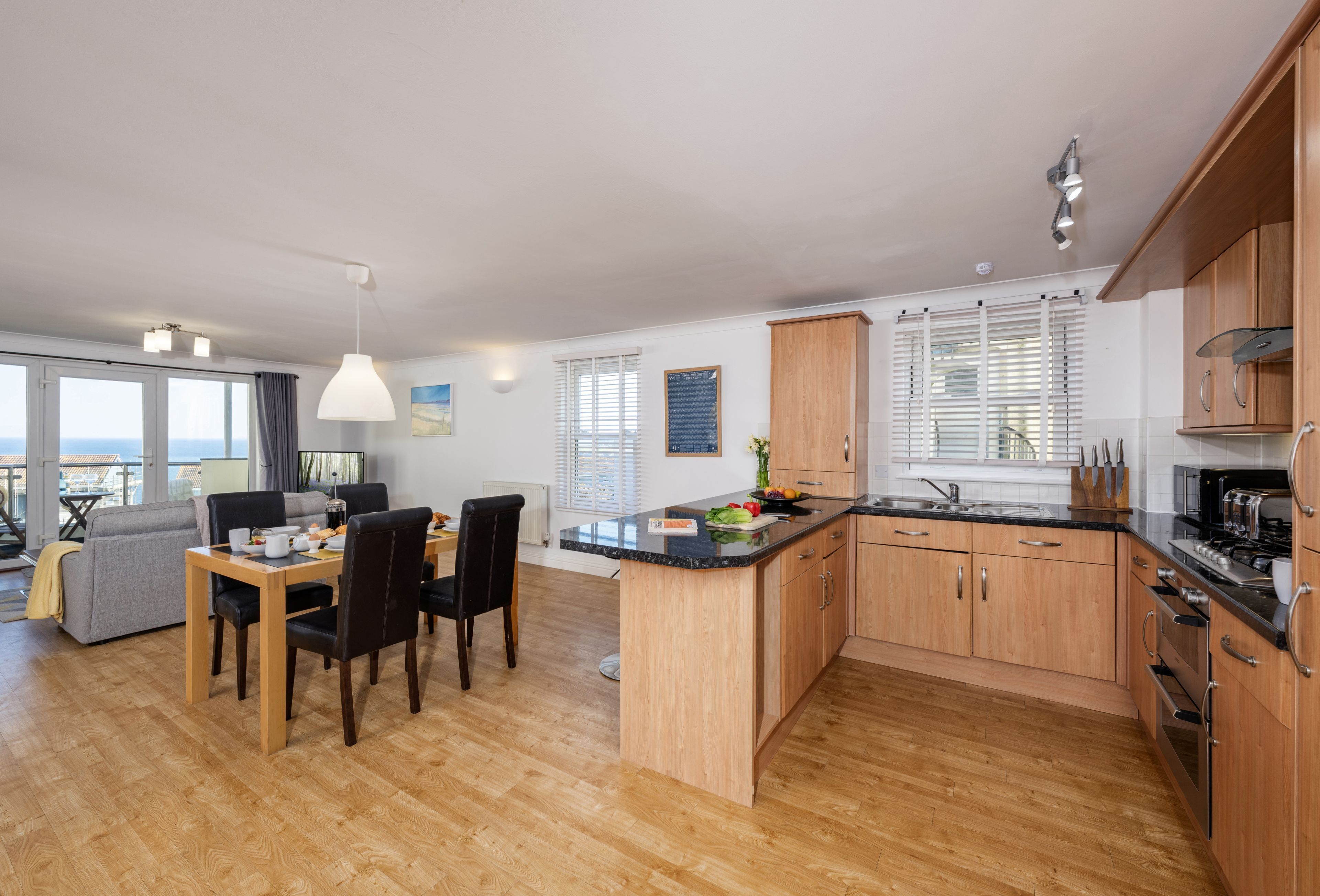 A modern kitchen with wooden cabinets, a dining area with a table and chairs, and a view of the city through large windows.