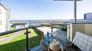 A balcony with a view of the sea, a bottle, two glasses, and a hat on a wooden table. - 8 Spinnakers, a charming two-bedroom apartment located in Pentire (Newquay)