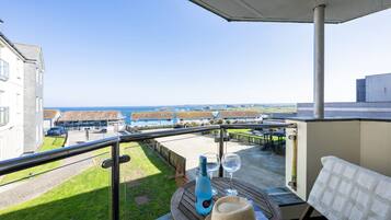 A balcony with a view of the sea, a bottle, two glasses, and a hat on a wooden table.