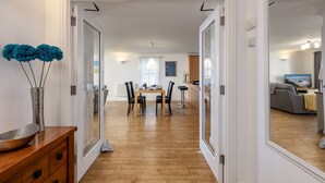 A modern interior with a dining area, wooden flooring, and a view into another room with a sofa and TV. - 8 Spinnakers, a charming two-bedroom apartment located in Pentire (Newquay)