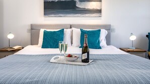 A neatly made bed with a tray of champagne, glasses, and a bowl of fruit. - 8 Spinnakers, a charming two-bedroom apartment located in Pentire (Newquay)