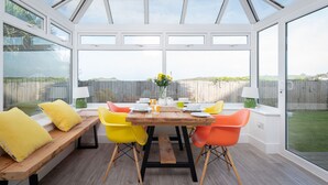 Un invernadero con una mesa de madera, sillas de color amarillo brillante y naranja, y un banco.