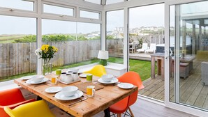 Un invernadero con una mesa de madera dispuesta para el desayuno, ventanas amplias y vistas al campo.