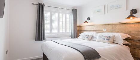 A bedroom with a bed, a window with curtains, a wall-mounted lamp, and a wooden headboard.