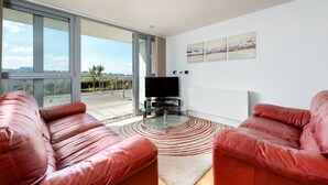 Una sala moderna con sofás de cuero, una mesa de centro de vidrio, un televisor de pantalla plana y un ventanal con vistas al exterior.