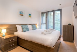 A neatly made bed with a wooden headboard, a nightstand with a lamp, and two framed pictures on the wall.