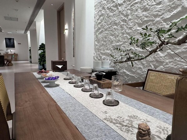 A modern dining area with a long wooden table, clear glassware, and a textured wall. - MingShanshui Shiguang Homestay (Fuzhou)