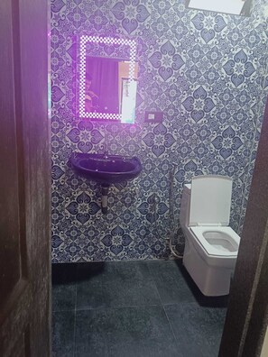 A bathroom with a geometric-patterned wall, featuring a toilet and a sink with a mirror above.