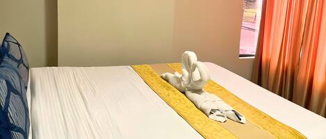 A neatly made bed with a white and yellow bedspread, a folded white towel, and a blue pillow.