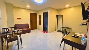 Une chambre d’hôtel avec un canapé, une table à manger avec des chaises, un téléviseur fixé au mur et une salle de bain visible à travers une porte ouverte.
