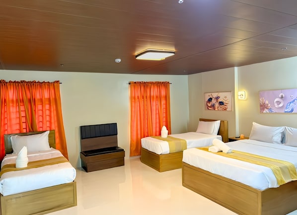 A hotel room with four beds, orange curtains, a wooden ceiling, and artwork on the walls.