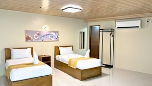 Une chambre d’hôtel avec deux lits en bois, un tableau au mur, un appareil de climatisation et une armoire.