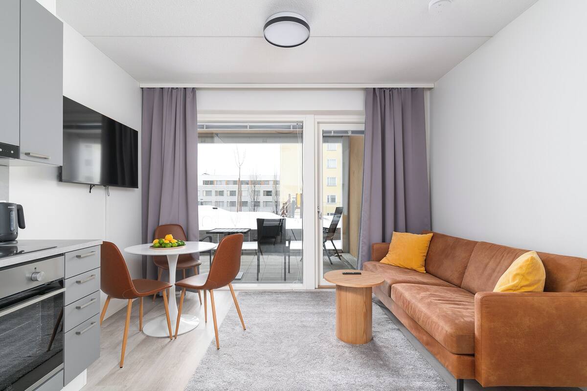 Un apartamento moderno con cocina, comedor y sala de estar. Incluye un sofá, una mesa de centro y un televisor montado en la pared.